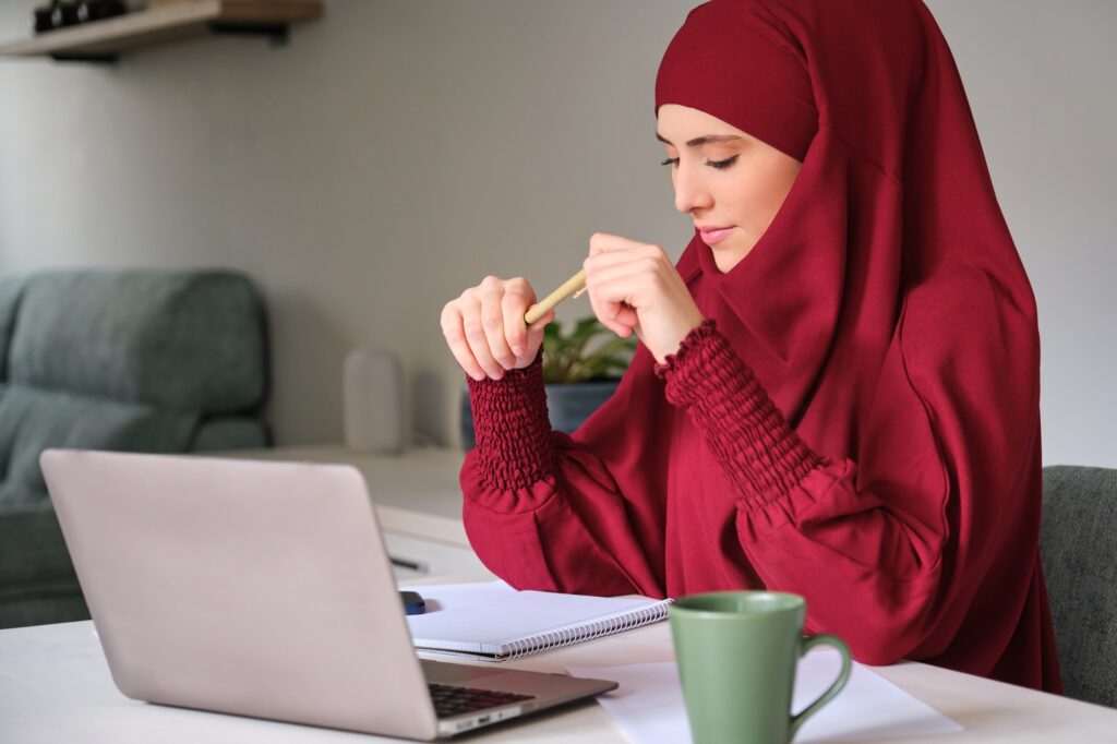 Muslim young woman in hijab using laptop at home.