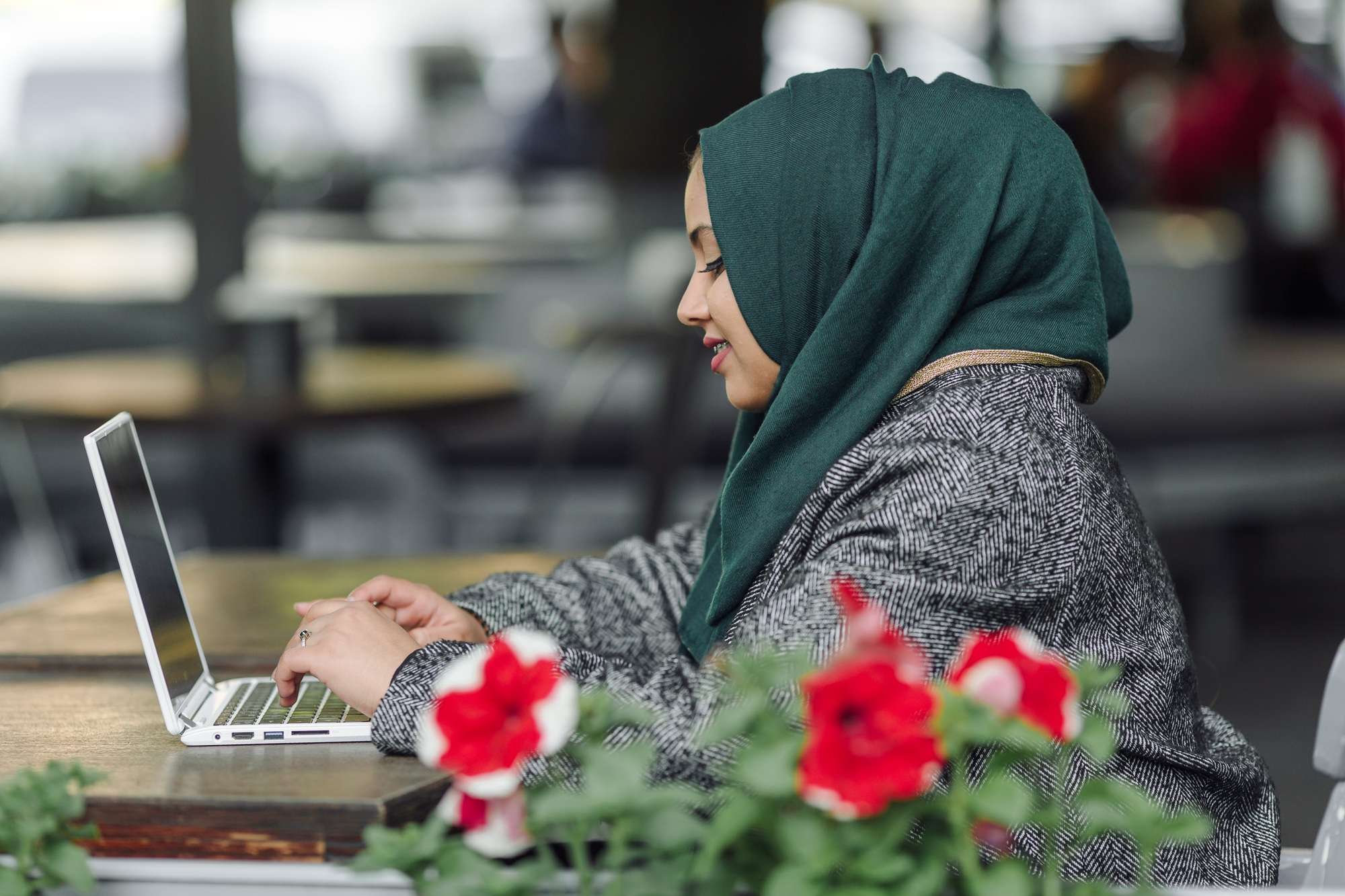 Portrait of a muslim girl in a green hijab with a laptop in the street cafe